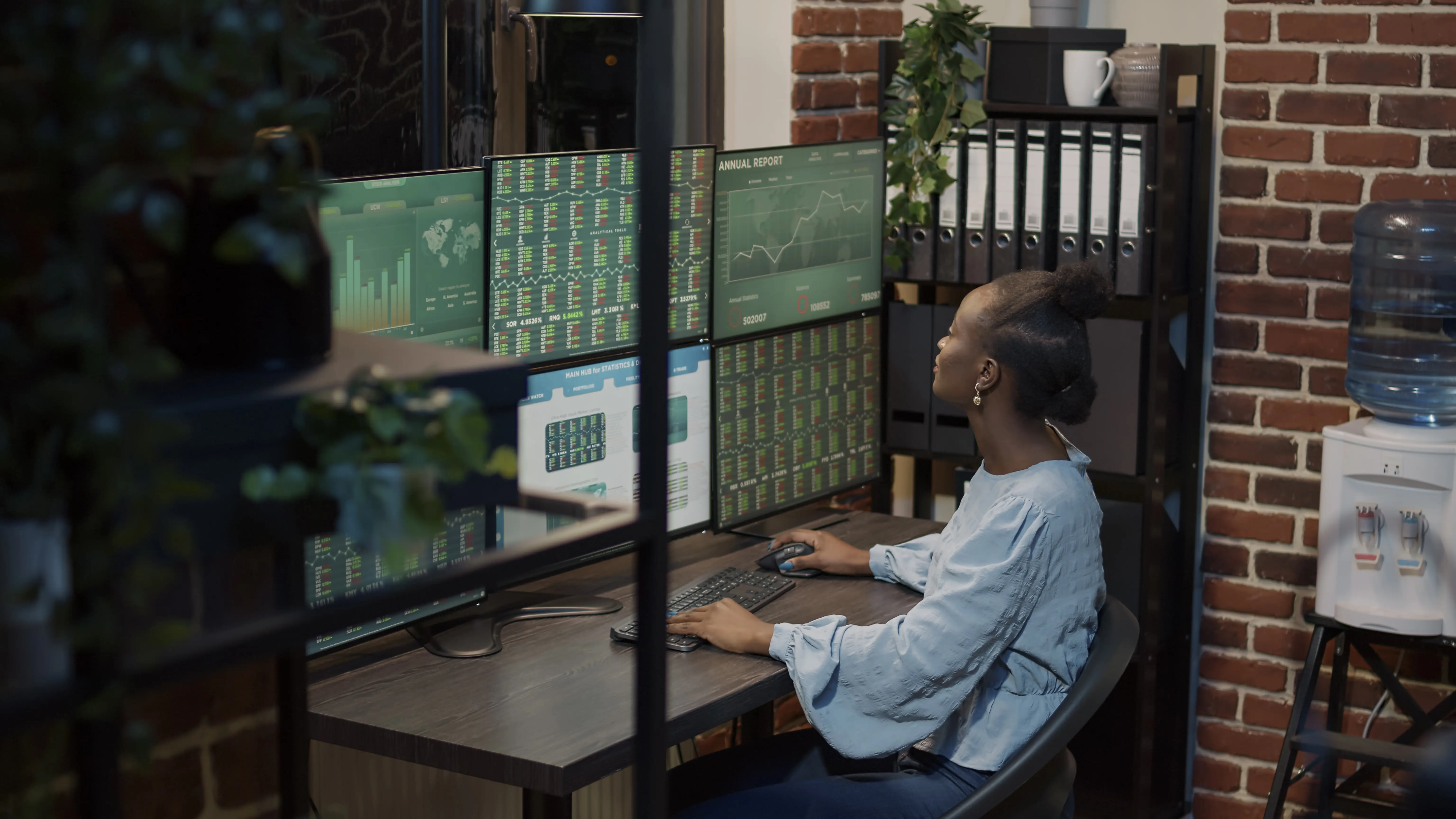 Afroamerikanische Frau analysiert Aktienmarktinvestitionen und Verkaufstransaktionen an der Börse anhand statistischer Diagramme und Grafiken auf mehreren Monitoren. Eine Börsenmaklerin nutzt Finanz- und Bankkurse, um Gewinne zu teilen.